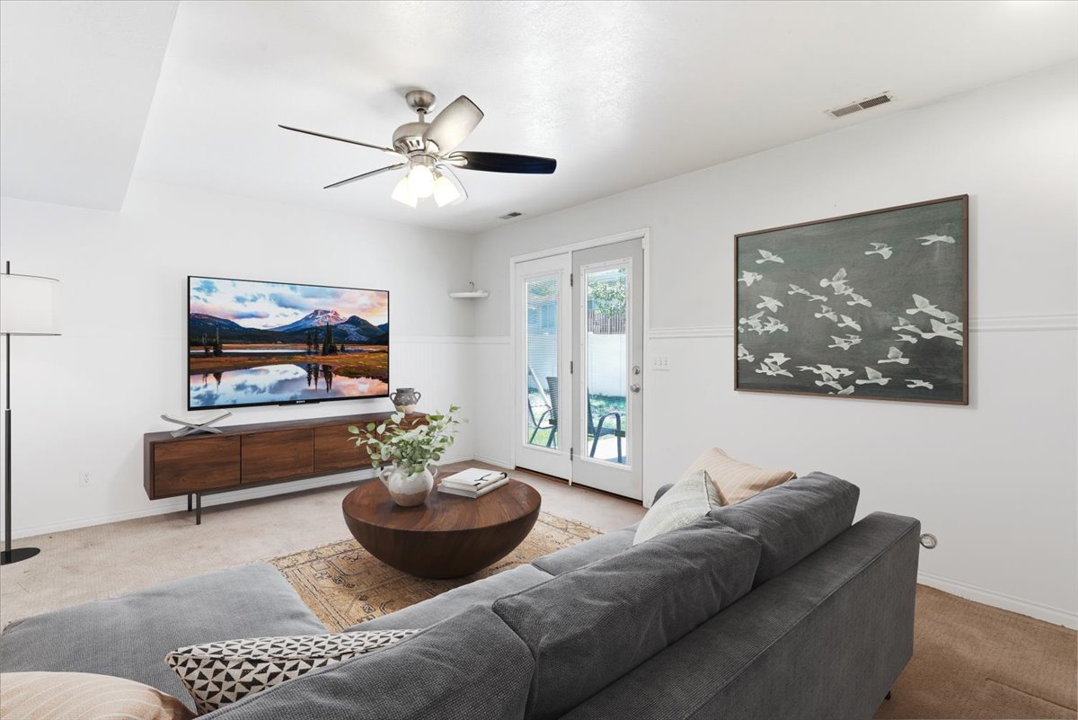 Living area featuring white walls, carpeting, and a ceiling fan with integrated lighting