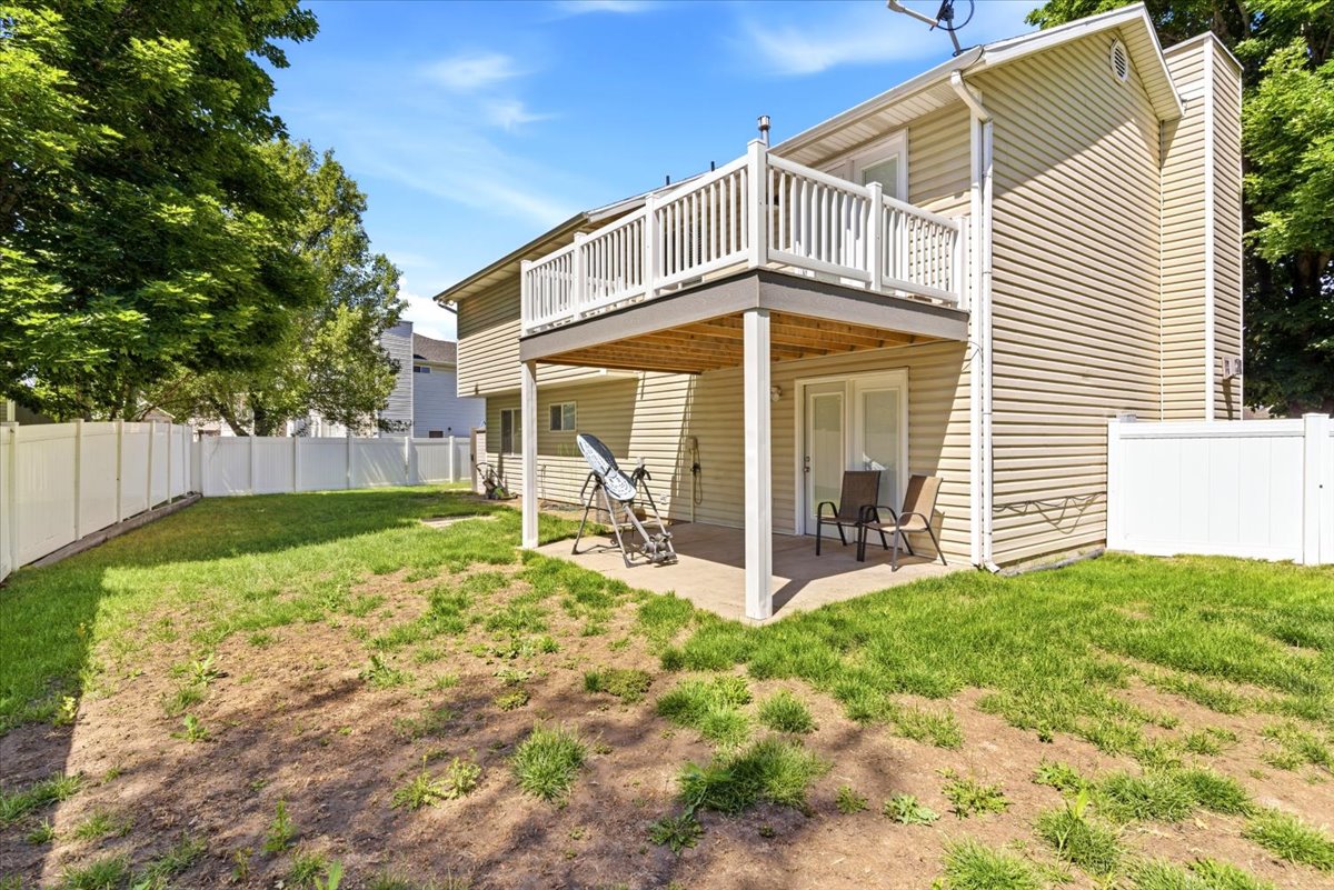 Rear exterior featuring a second-story balcony with white railings, a ground-level patio, and a fenced backyard