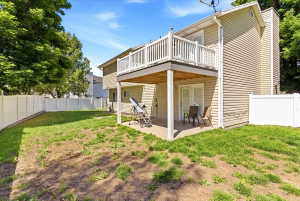 Rear exterior featuring a second-story balcony with white railings, a ground-level patio, and a fenced backyard