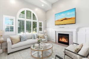 Living room featuring an arched window with plantation shutters, a white paneled fireplace with a white brick surround, and light wood-finish flooring