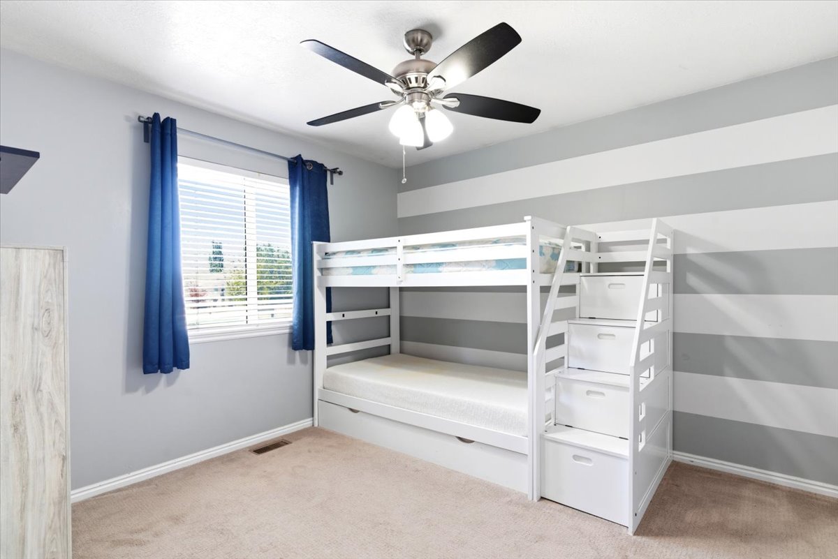 Spacious room featuring neutral carpet flooring, a window with horizontal blinds, and a ceiling fan with integrated lighting
