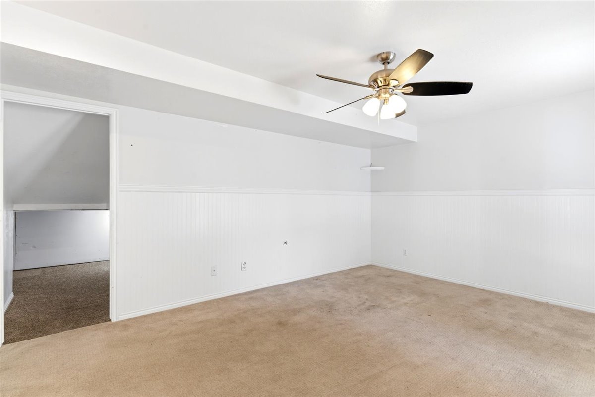 Carpeted room featuring a ceiling fan with integrated lighting, white walls, and wainscoting