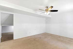 Carpeted room featuring a ceiling fan with integrated lighting, white walls, and wainscoting