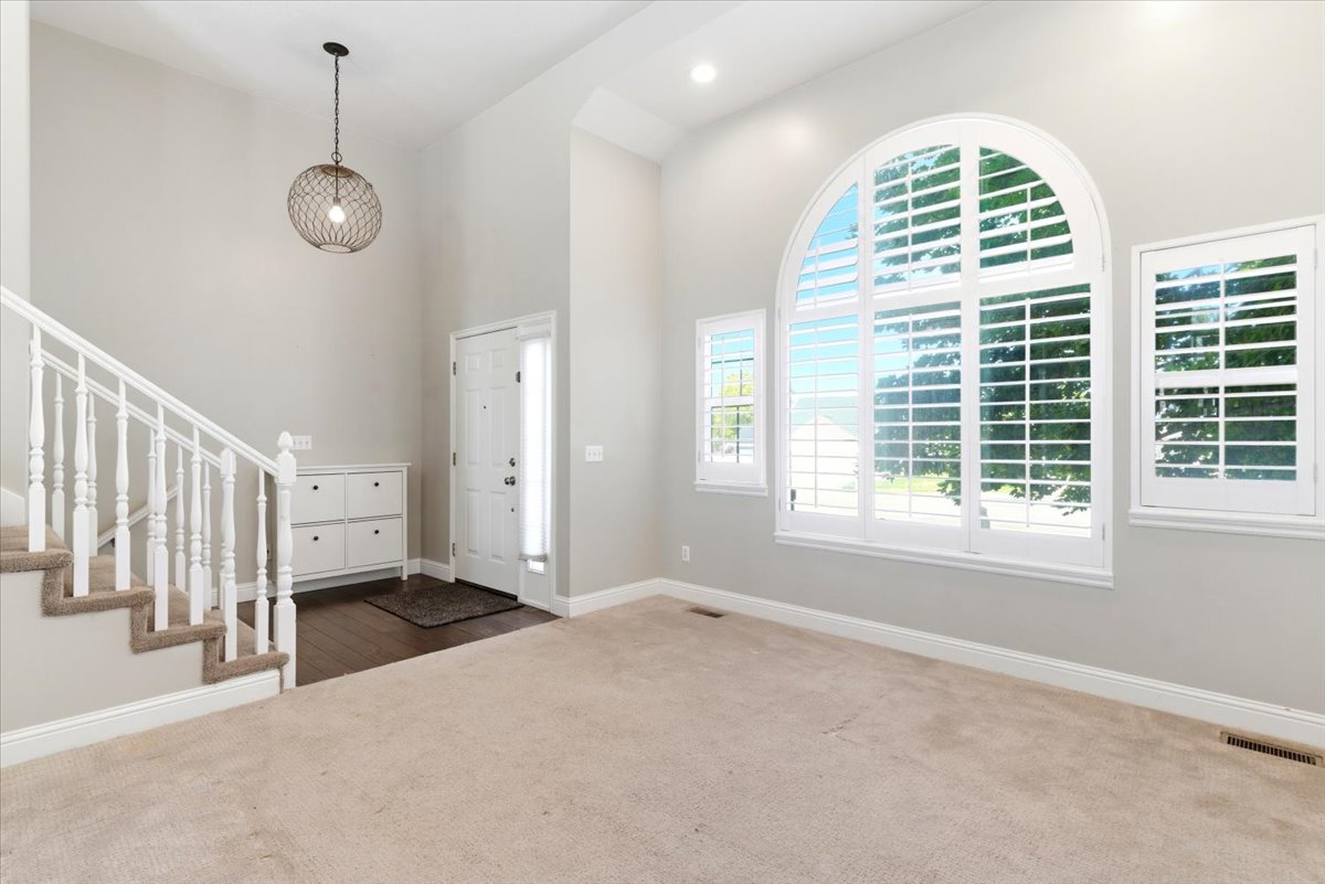 Two-story entryway featuring an arched window with white plantation shutters, a complementary side window, and a white front door with a sidelight