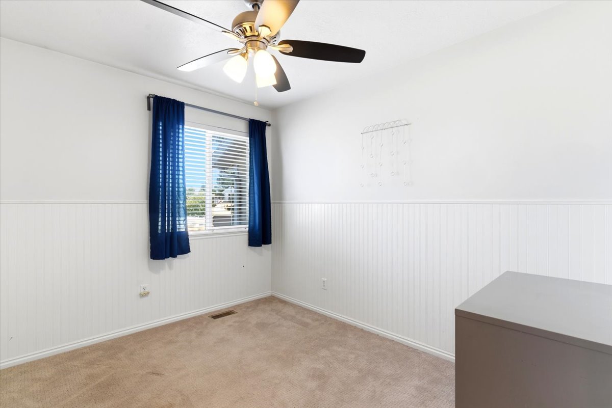 Interior room featuring a ceiling fan with integrated lighting, a window with horizontal blinds, wainscoting along the lower walls, and carpet flooring