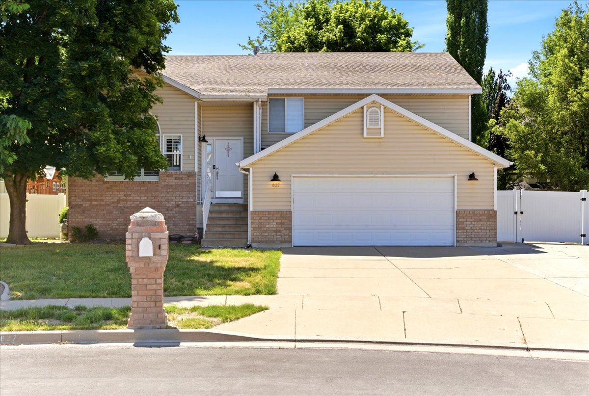 Two-story residence featuring light beige siding, brick accents, a two-car garage, and a white privacy fence