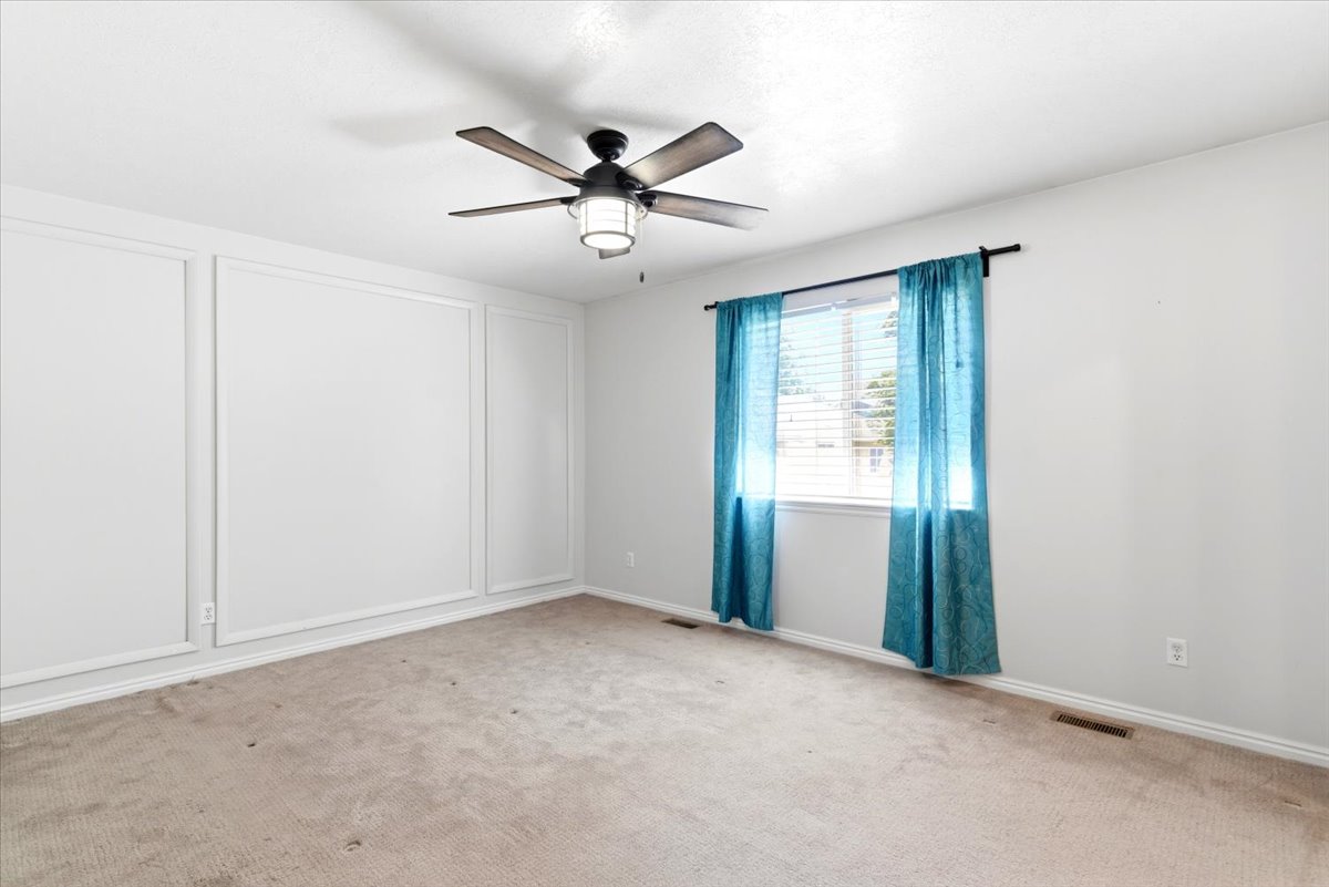 Spacious room featuring a ceiling fan with integrated lighting, a large window with blinds, and decorative wall paneling