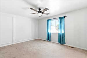 Spacious room featuring a ceiling fan with integrated lighting, a large window with blinds, and decorative wall paneling