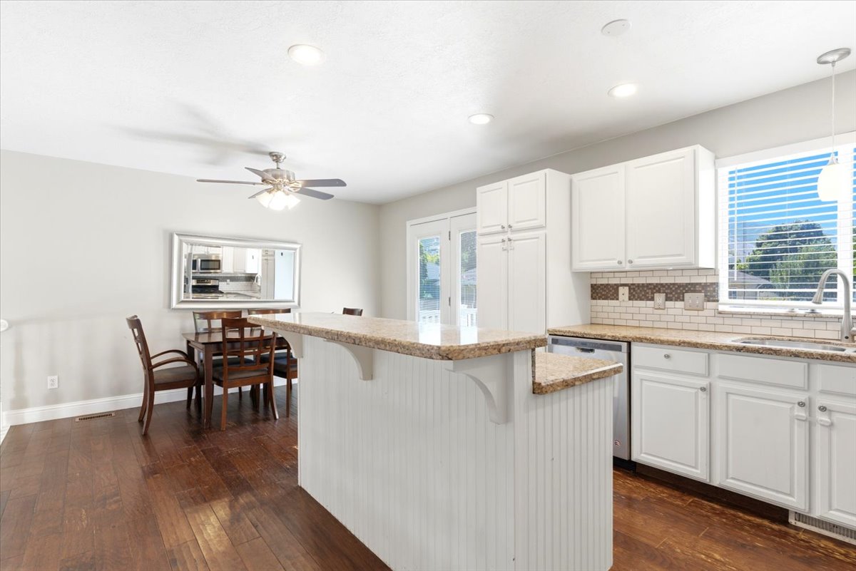 Open-concept kitchen and dining area featuring a breakfast bar with beadboard paneling, white cabinetry, granite countertops, wood-finish flooring, and recessed lighting