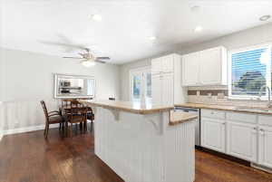 Open-concept kitchen and dining area featuring a breakfast bar with beadboard paneling, white cabinetry, granite countertops, wood-finish flooring, and recessed lighting