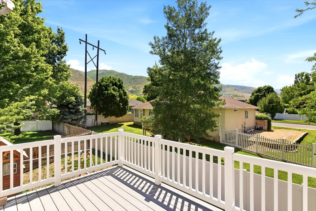 Upper-level deck featuring composite decking, white railing, mature trees, and a mountain backdrop