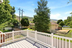 Upper-level deck featuring composite decking, white railing, mature trees, and a mountain backdrop