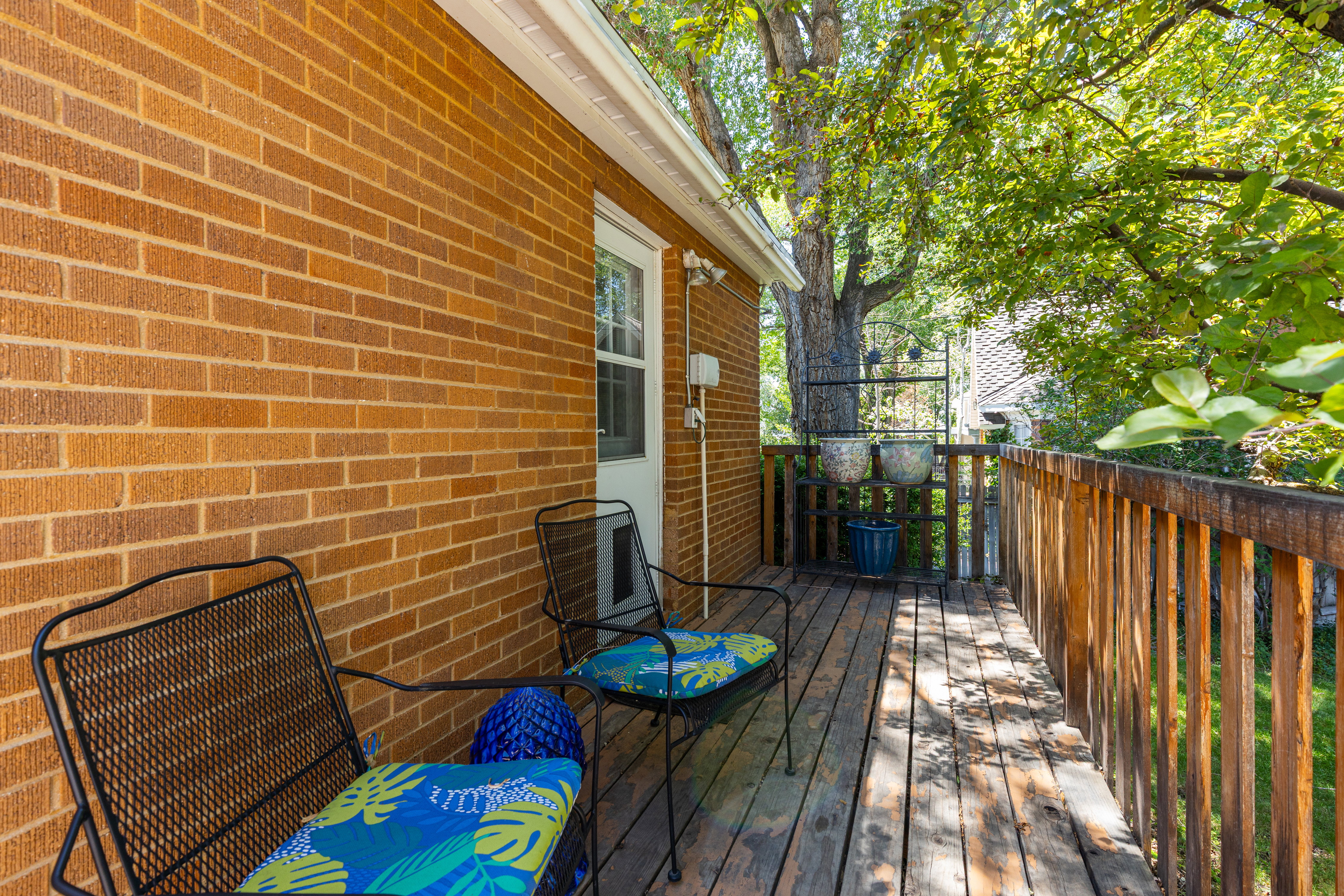 Outdoor wooden deck featuring a natural wood railing, a solid brick exterior wall, and a white exterior door