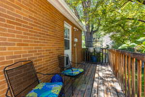Outdoor wooden deck featuring a natural wood railing, a solid brick exterior wall, and a white exterior door