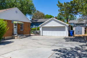 Expansive concrete driveway featuring a two-car garage with white siding and a separate storage shed