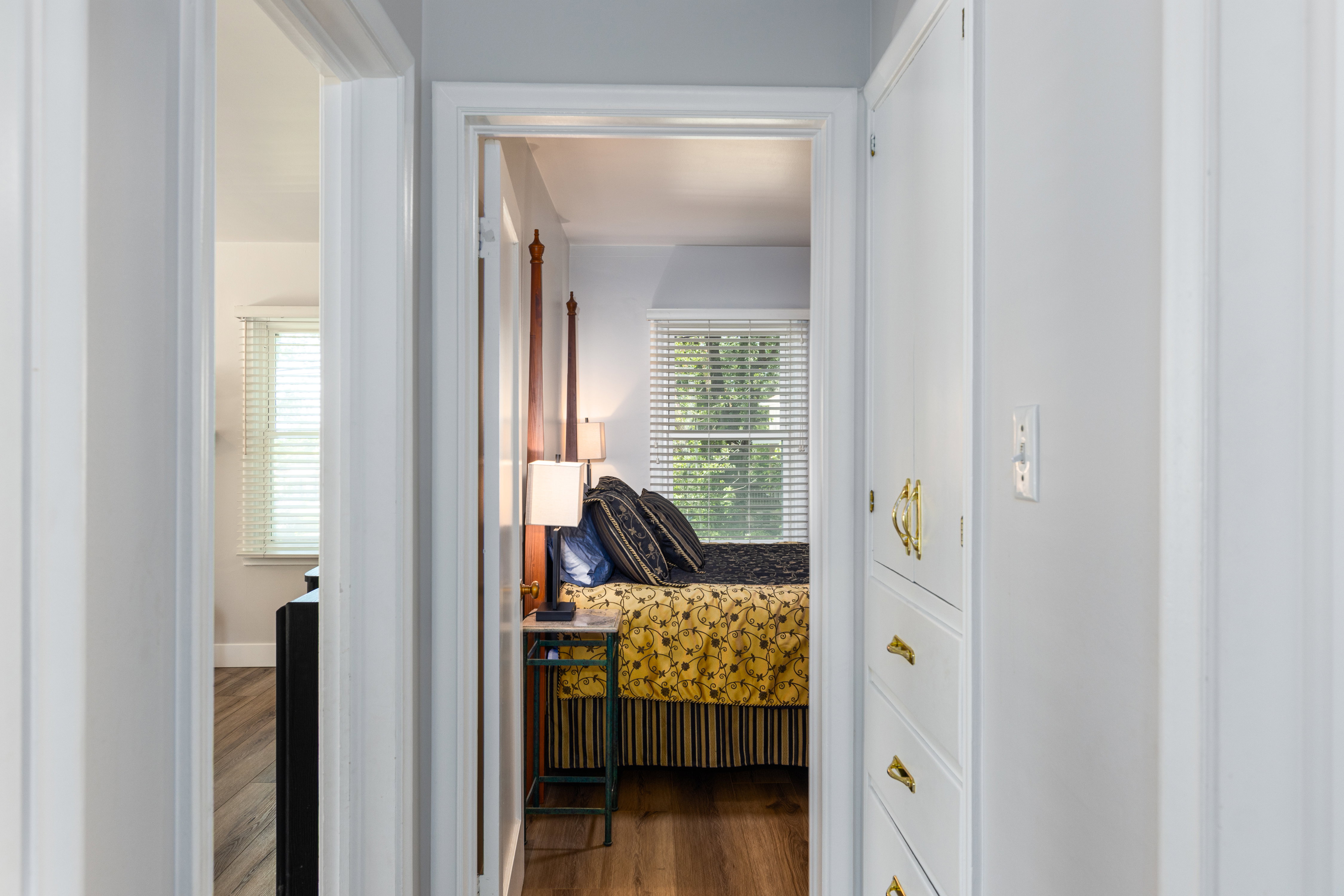 Hallway with white walls and wood-finish flooring, featuring a built-in white cabinetry unit with brass hardware
