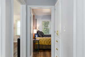Hallway with white walls and wood-finish flooring, featuring a built-in white cabinetry unit with brass hardware