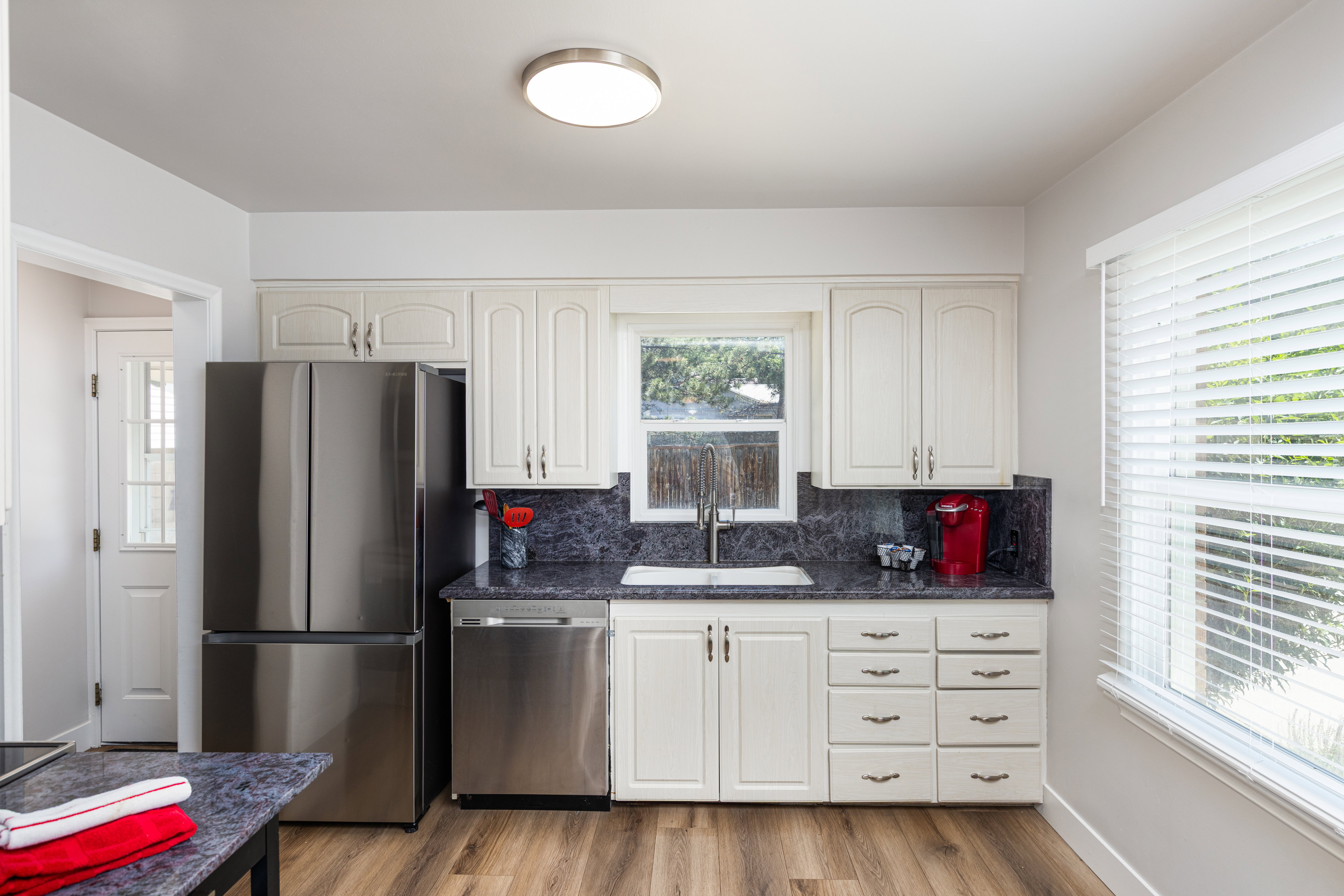 Kitchen featuring white cabinetry, dark stone countertops, stainless steel appliances, and wood-finish flooring