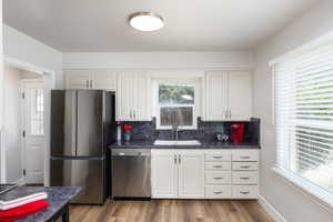 Kitchen featuring white cabinetry, dark stone countertops, stainless steel appliances, and wood-finish flooring