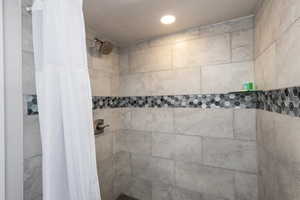 Walk-in shower featuring large format tile walls, a decorative hexagonal mosaic tile band, a recessed niche with hexagonal tile, a glass shelf, and a ceiling-mounted recessed light