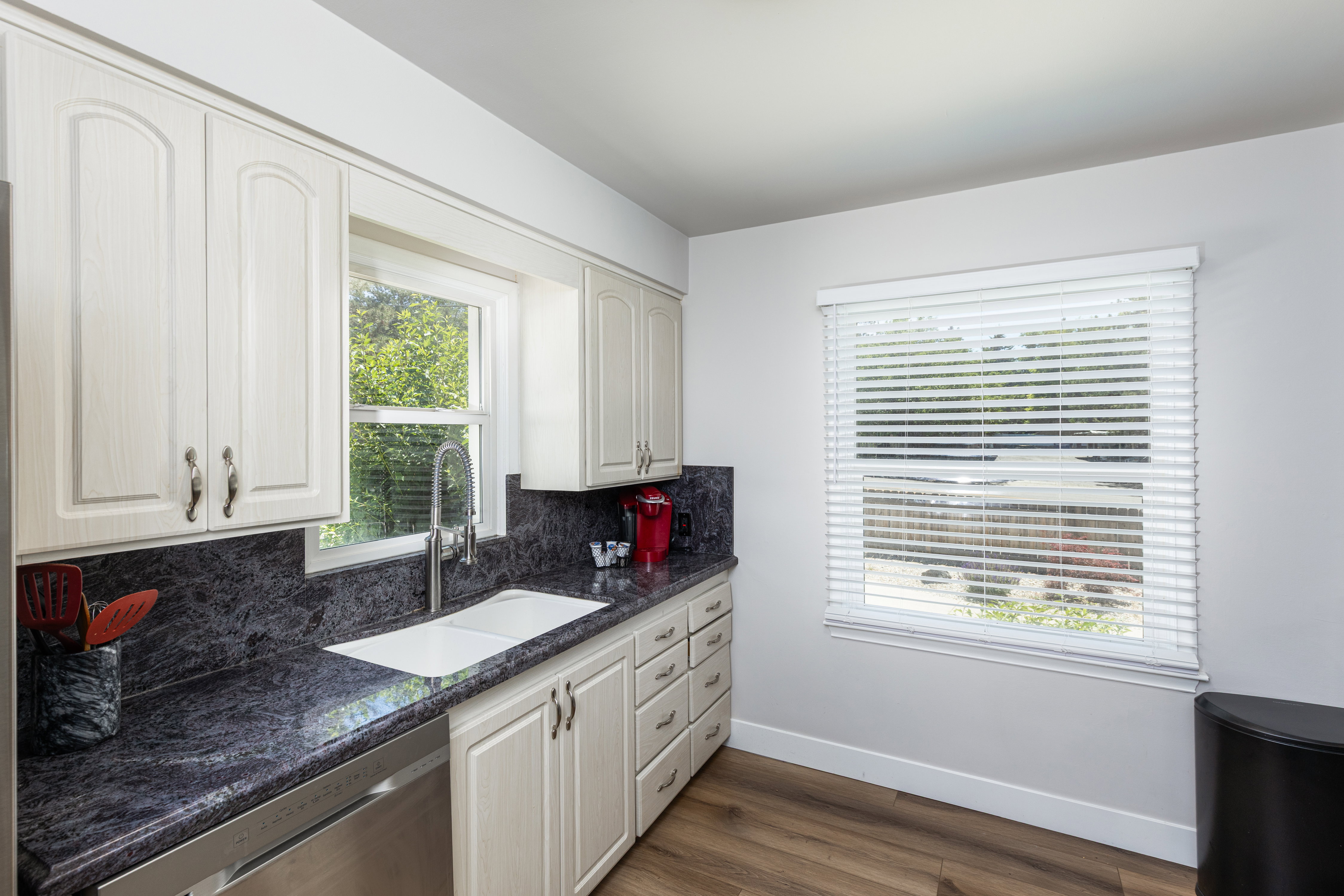 Kitchen featuring light-toned cabinetry, dark patterned countertops, a double basin sink with a gooseneck faucet, and stainless steel dishwasher