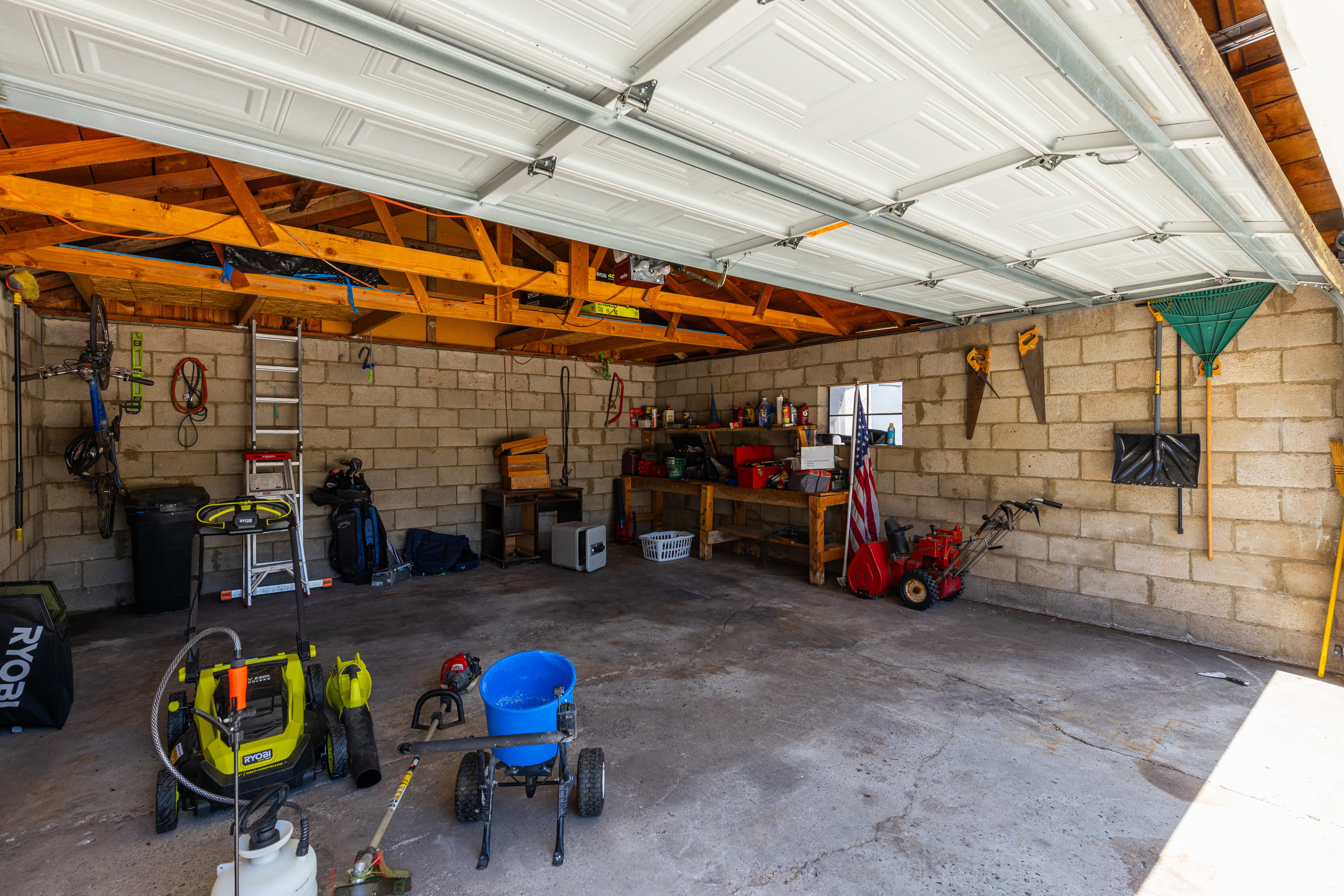 Spacious garage featuring concrete block walls, exposed wood beam ceiling, a single window, and a durable concrete floor