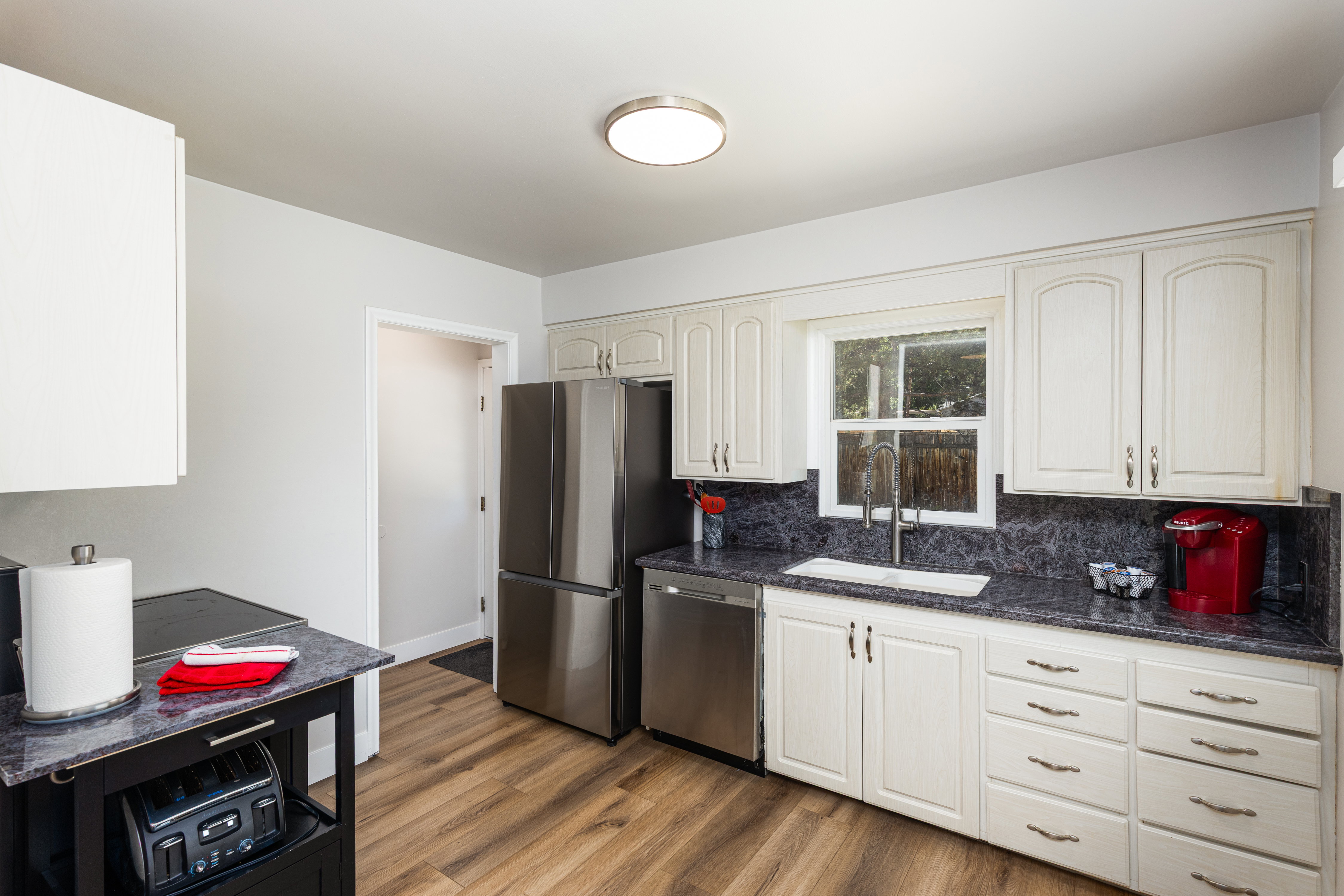 Kitchen featuring white cabinetry, dark patterned countertops, stainless steel appliances, wood-finish flooring, and a window above the sink