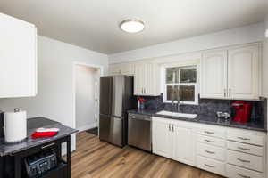 Kitchen featuring white cabinetry, dark patterned countertops, stainless steel appliances, wood-finish flooring, and a window above the sink
