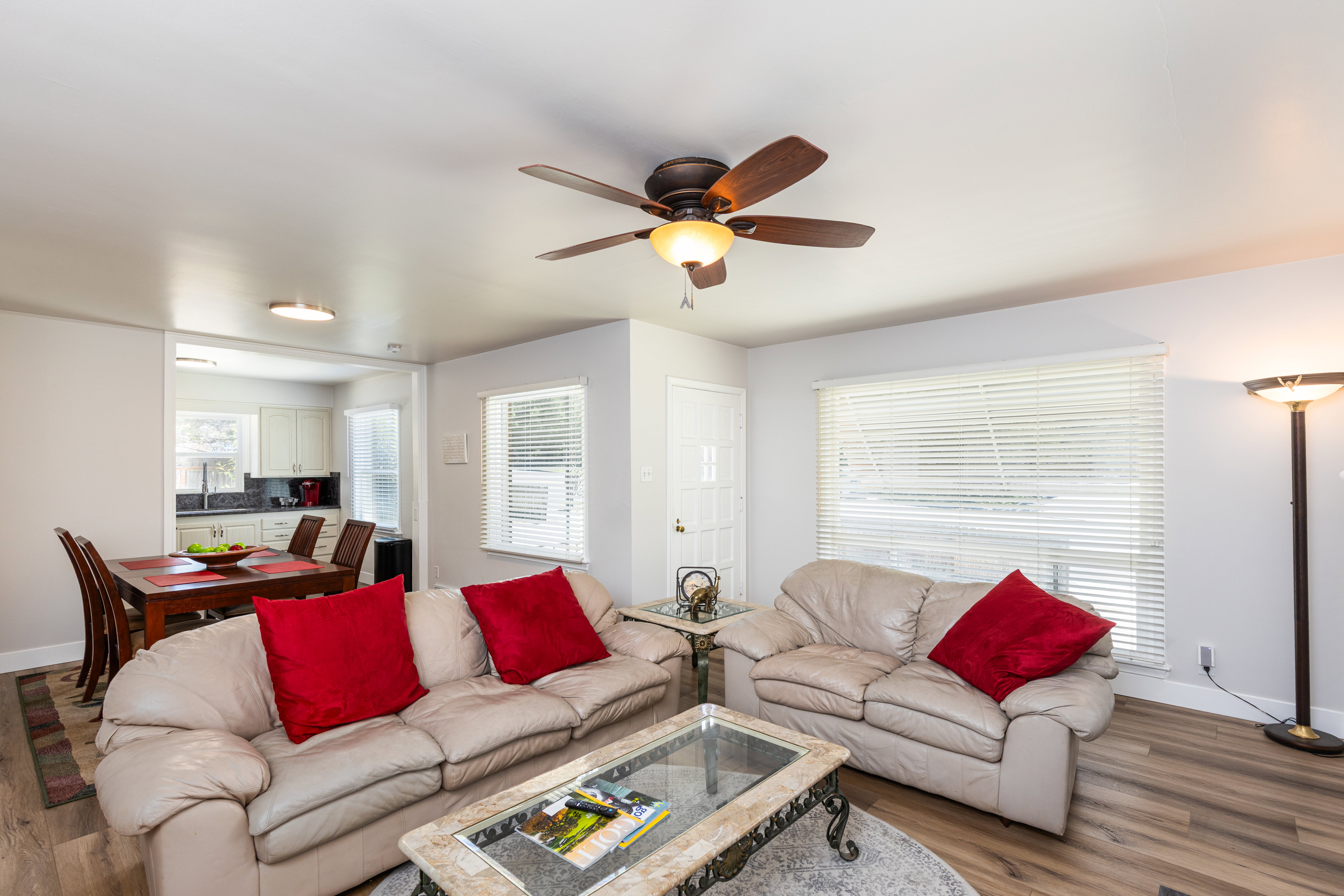 Open-concept living area featuring wood-finish flooring, a ceiling fan with integrated lighting, and white horizontal blinds