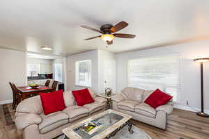 Open-concept living area featuring wood-finish flooring, a ceiling fan with integrated lighting, and white horizontal blinds