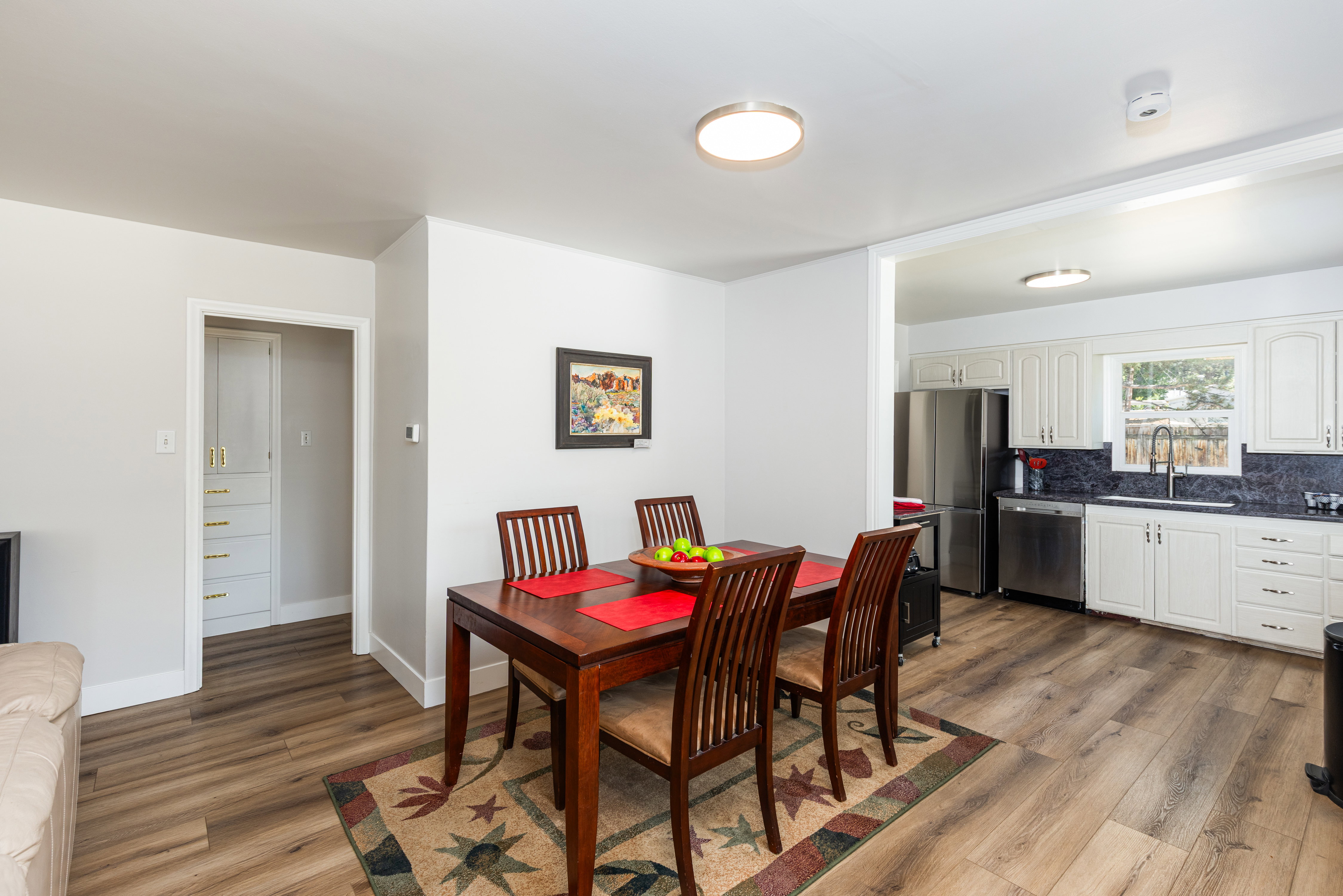 Open-concept living space featuring wood-finish flooring, a kitchen with white cabinetry and stainless steel appliances, and a built-in storage cabinet with gold-tone hardware