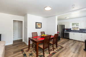 Open-concept living space featuring wood-finish flooring, a kitchen with white cabinetry and stainless steel appliances, and a built-in storage cabinet with gold-tone hardware