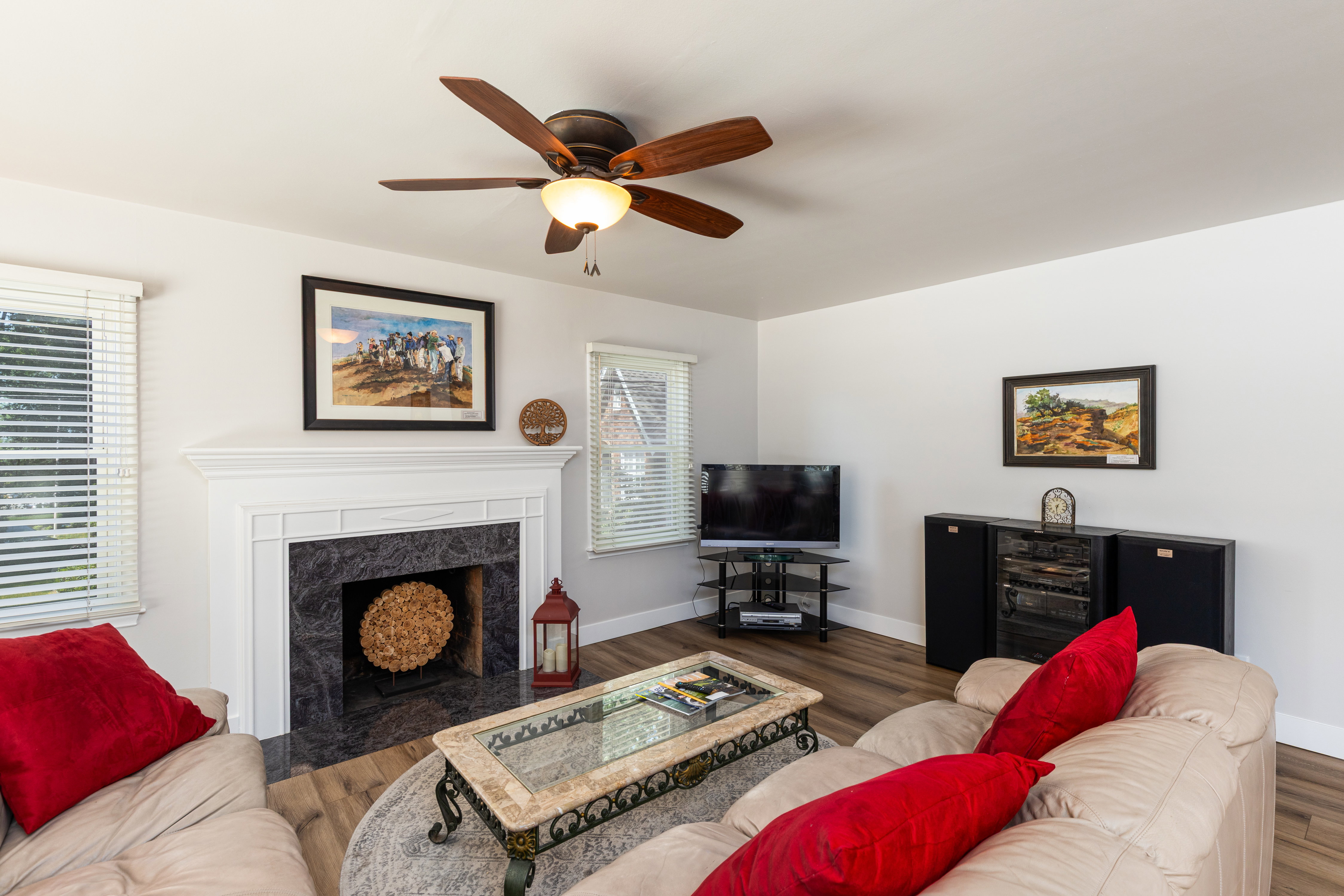 Living area featuring a white mantel fireplace with a dark stone surround, wood-finish flooring, and a ceiling fan with integrated lighting