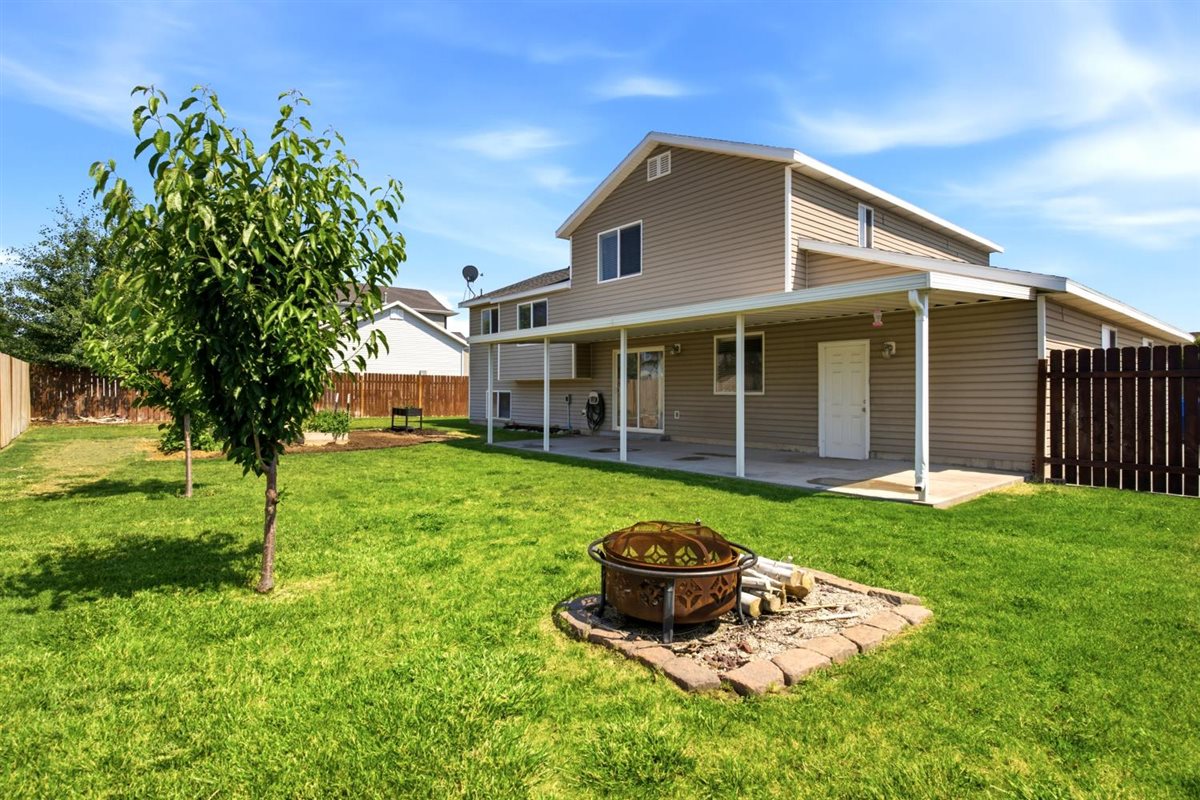 Expansive green lawn with a fire pit, mature trees, and a full-length covered patio