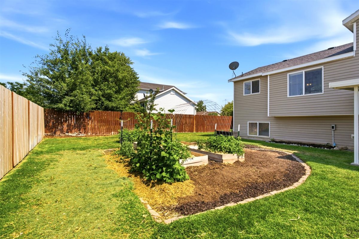 Expansive backyard featuring a manicured lawn, wood fencing, and raised garden beds