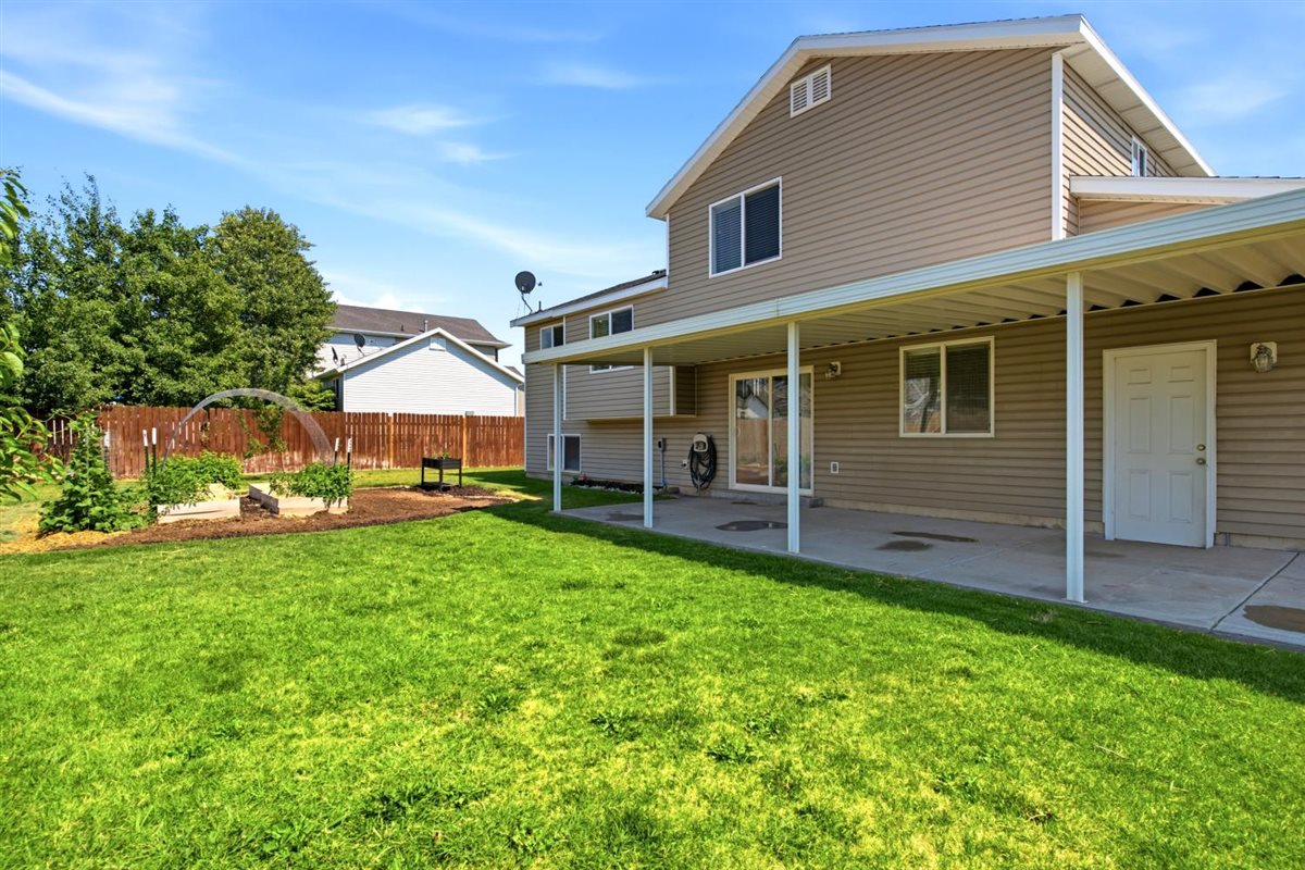 Spacious backyard featuring a covered patio, expansive lawn, raised garden beds, and a wood privacy fence