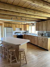 Spacious kitchen featuring light wood cabinetry, light countertops, wood-finish flooring, a central island with bar seating, and exposed wood ceiling beams