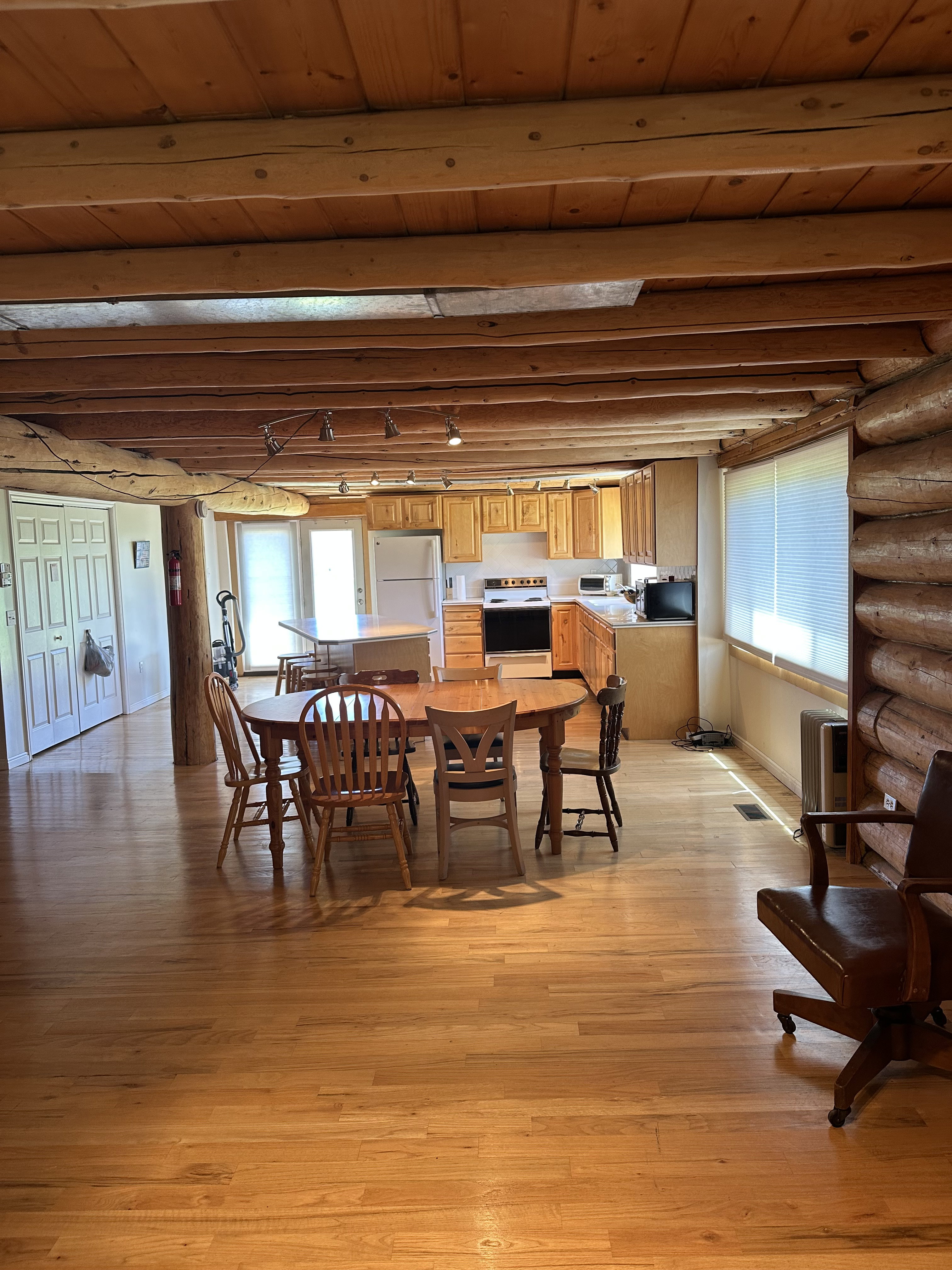 Open-concept living area with wood-finish flooring, exposed log beam ceiling, and log wall accents