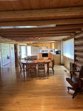 Open-concept living area with wood-finish flooring, exposed log beam ceiling, and log wall accents