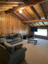 Carpeted living space featuring wood paneling and exposed wood beams