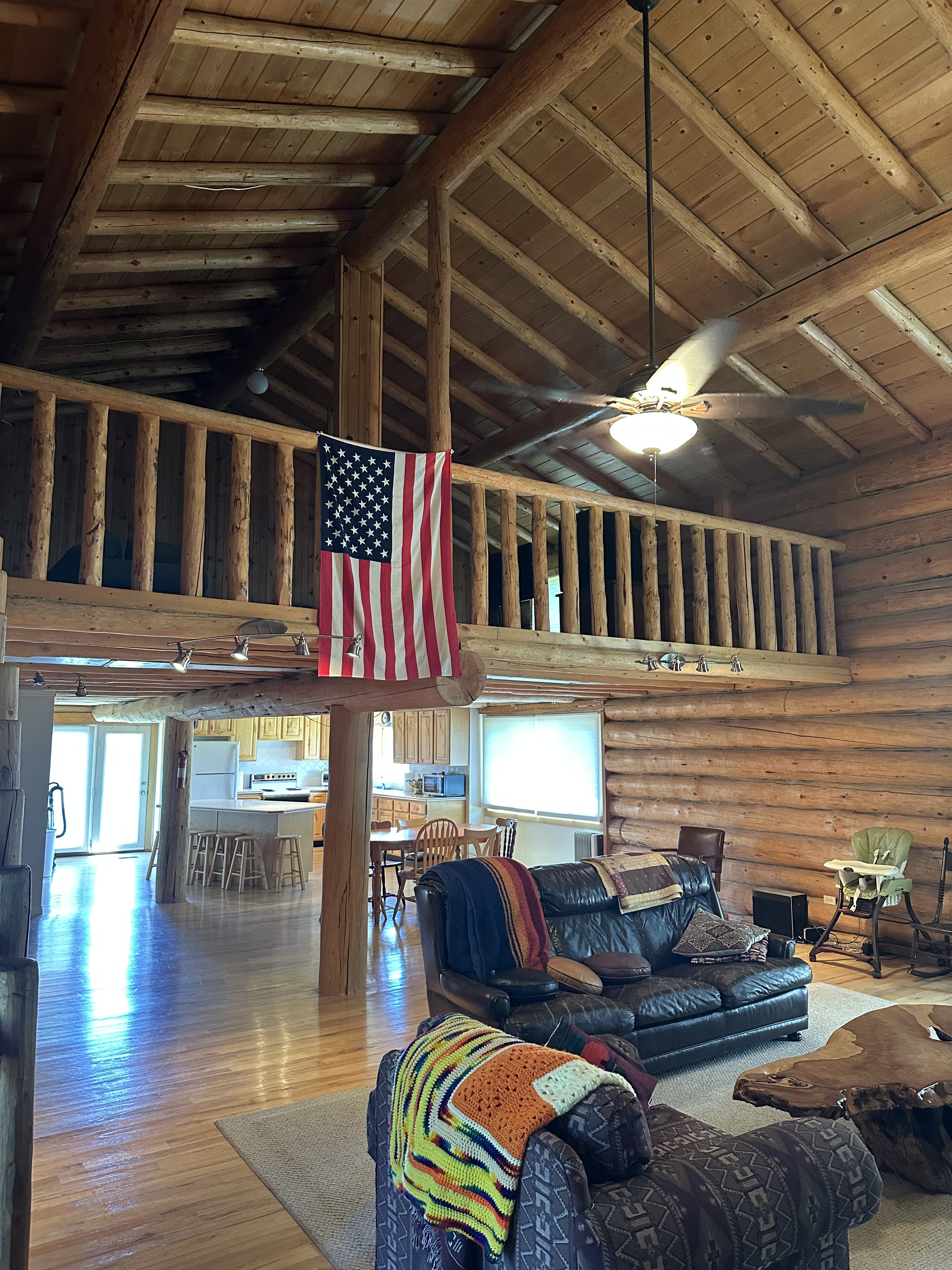 Spacious log cabin interior featuring a vaulted ceiling with exposed wood beams, a log railing balcony, and wood-finish flooring