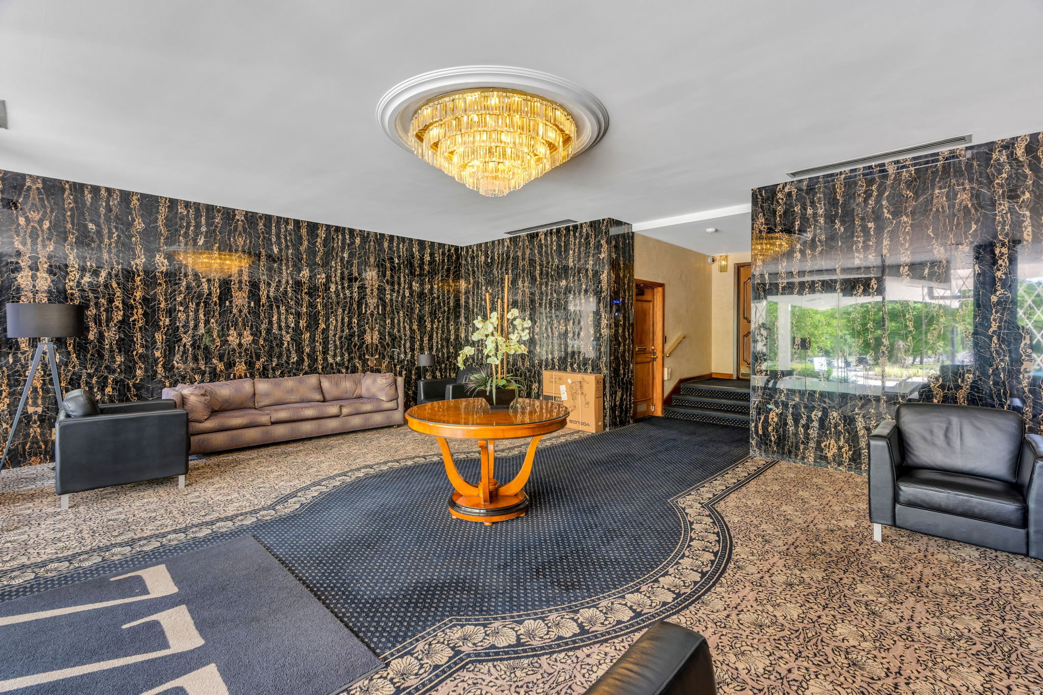 Lobby featuring a large crystal chandelier, patterned carpeting, black and gold wall paneling, and a polished wood central table