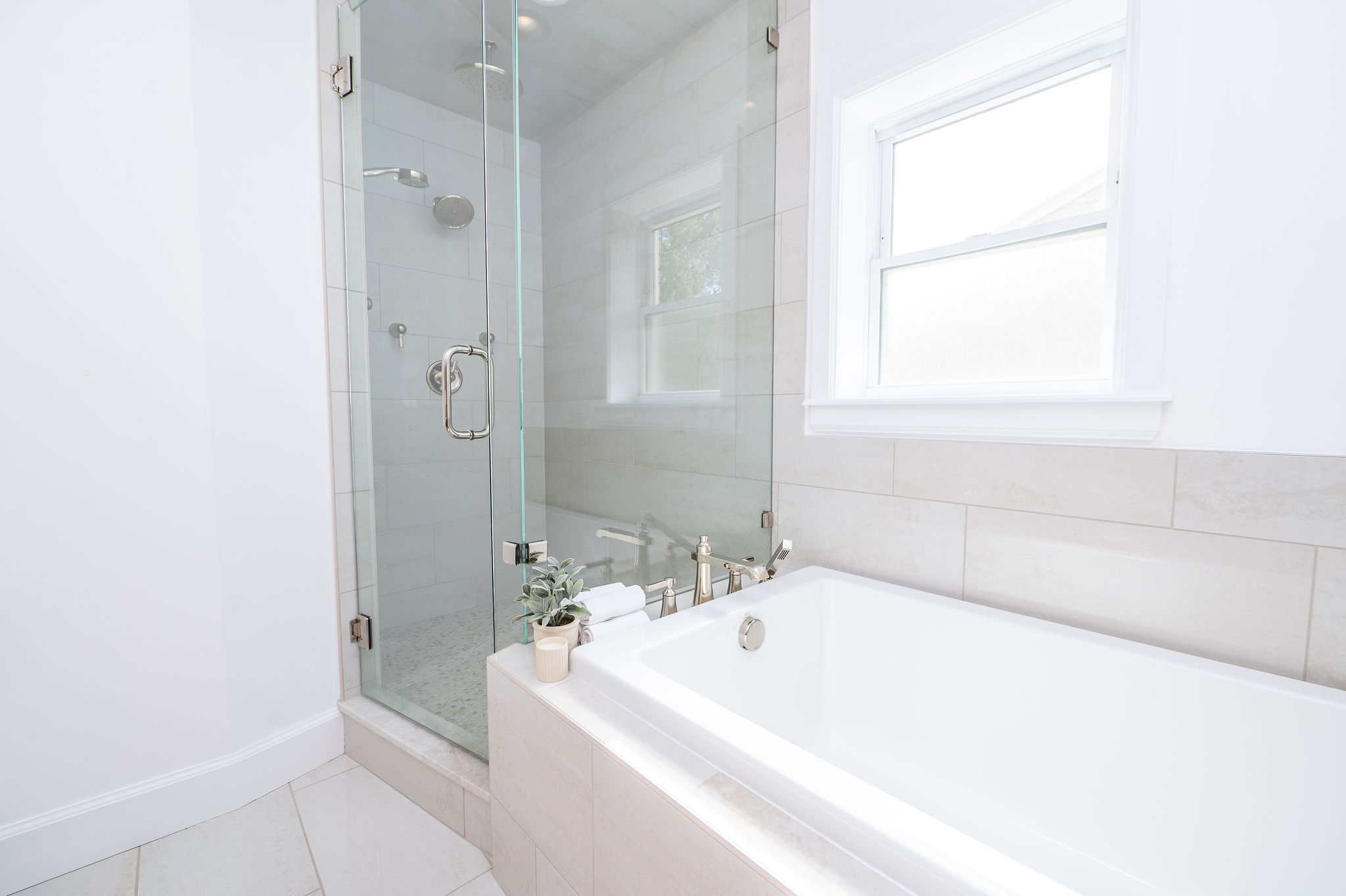Contemporary bathroom featuring a frameless glass shower enclosure, a built-in soaking tub, a window with white trim, and light-toned tile flooring