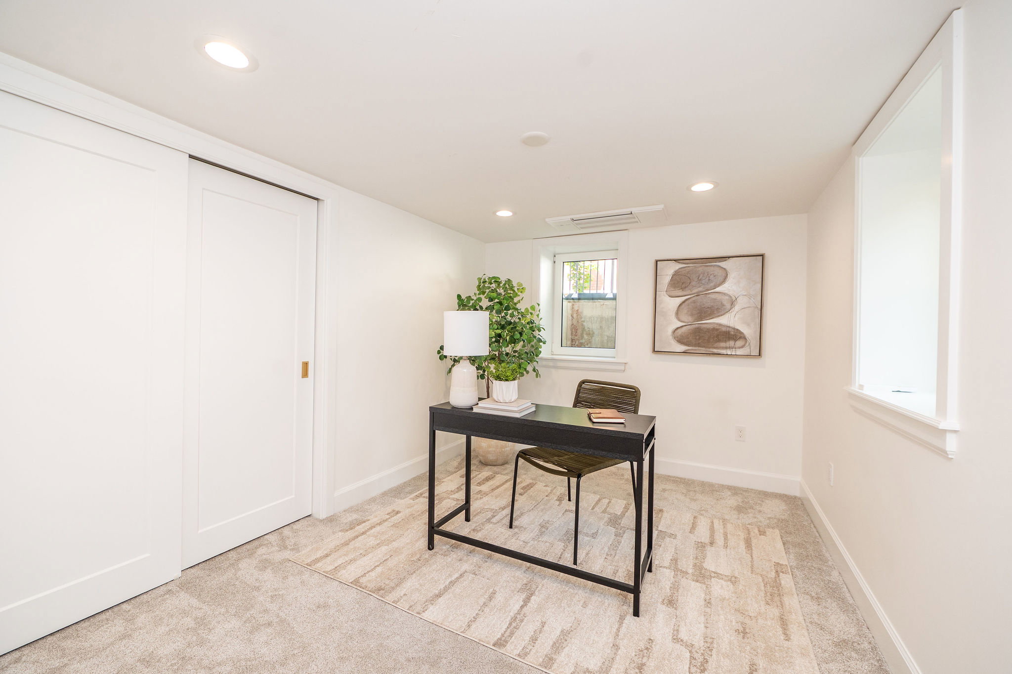 Recessed lighting illuminates this room, featuring light-colored carpeting, a window with a deep sill, and a white sliding panel door