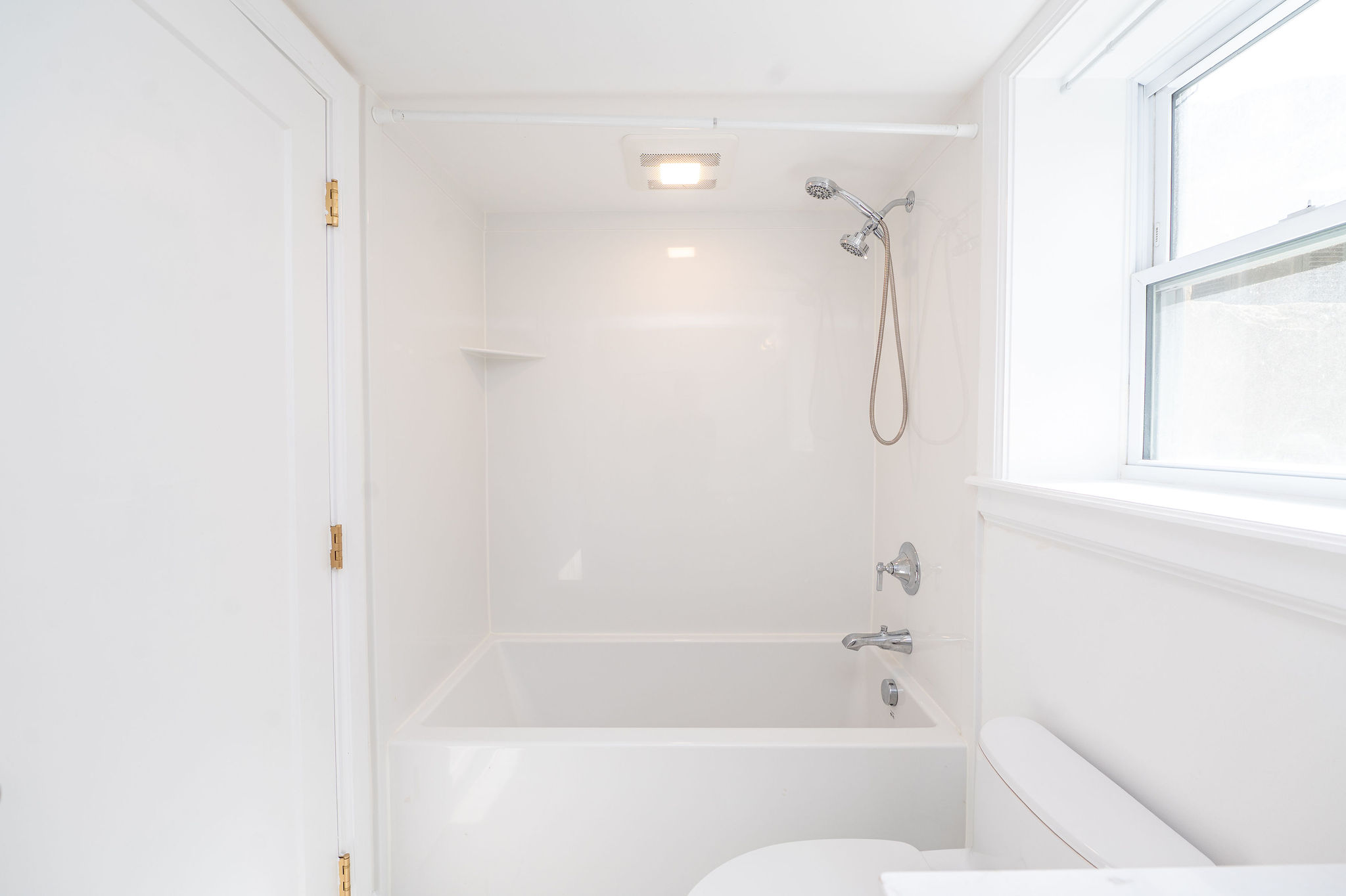 White bathroom featuring a bathtub and shower combination with a handheld showerhead, a toilet, and a window for natural light