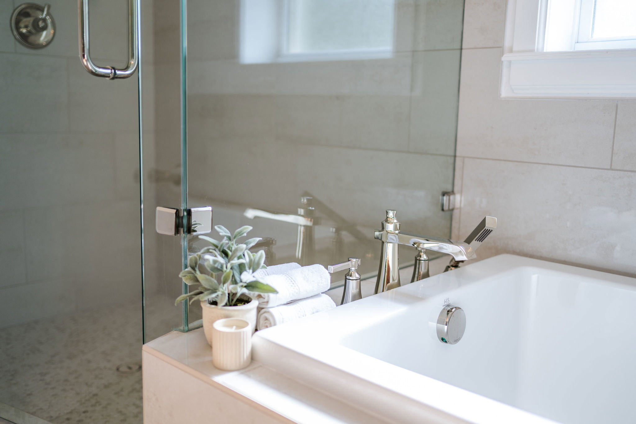 Bathtub featuring deck-mounted chrome faucet, integrated shower wand, and white tile surround