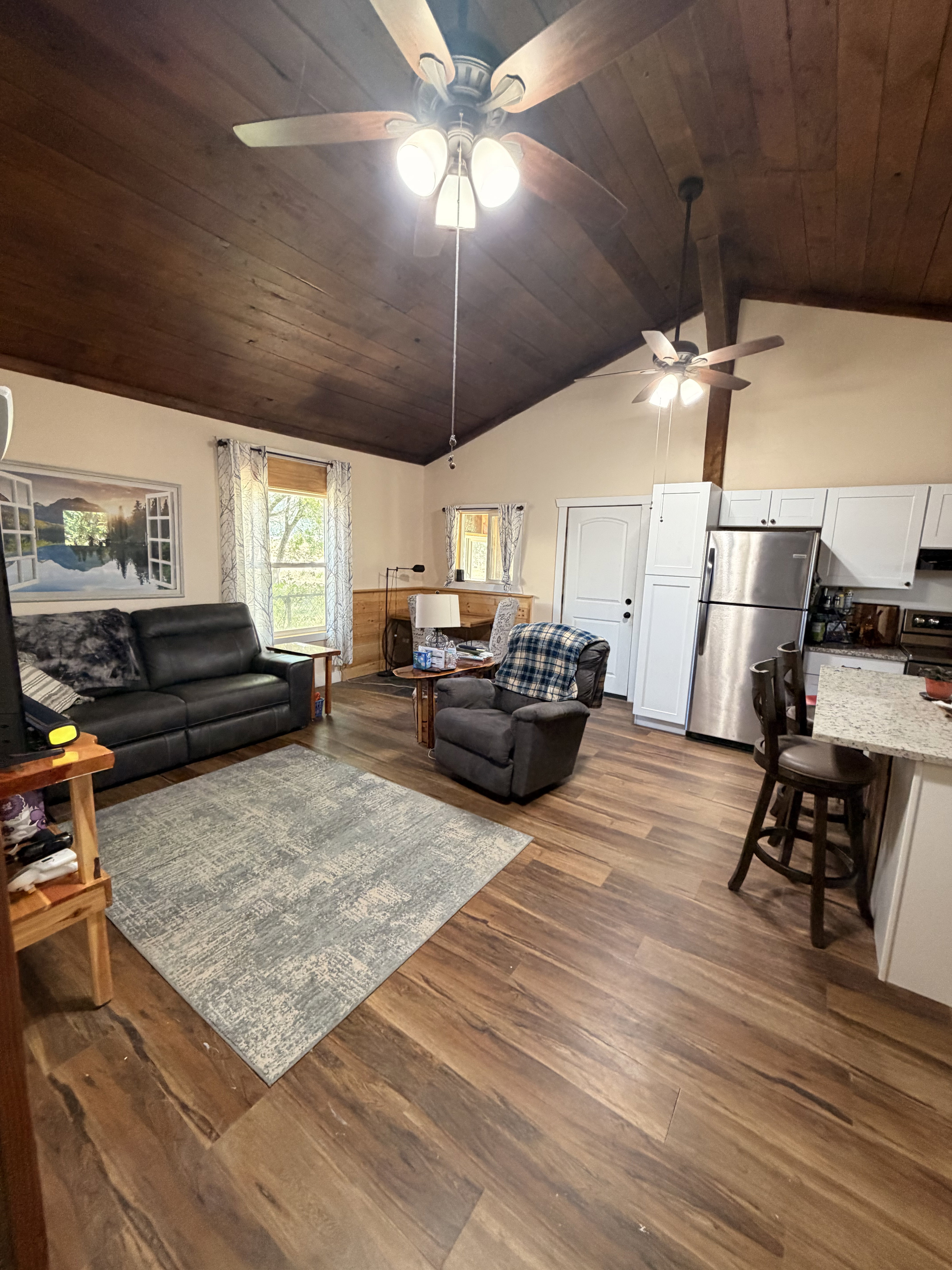 Spacious open-concept living area featuring wood-finish flooring, a vaulted wood-paneled ceiling, and multiple ceiling fans