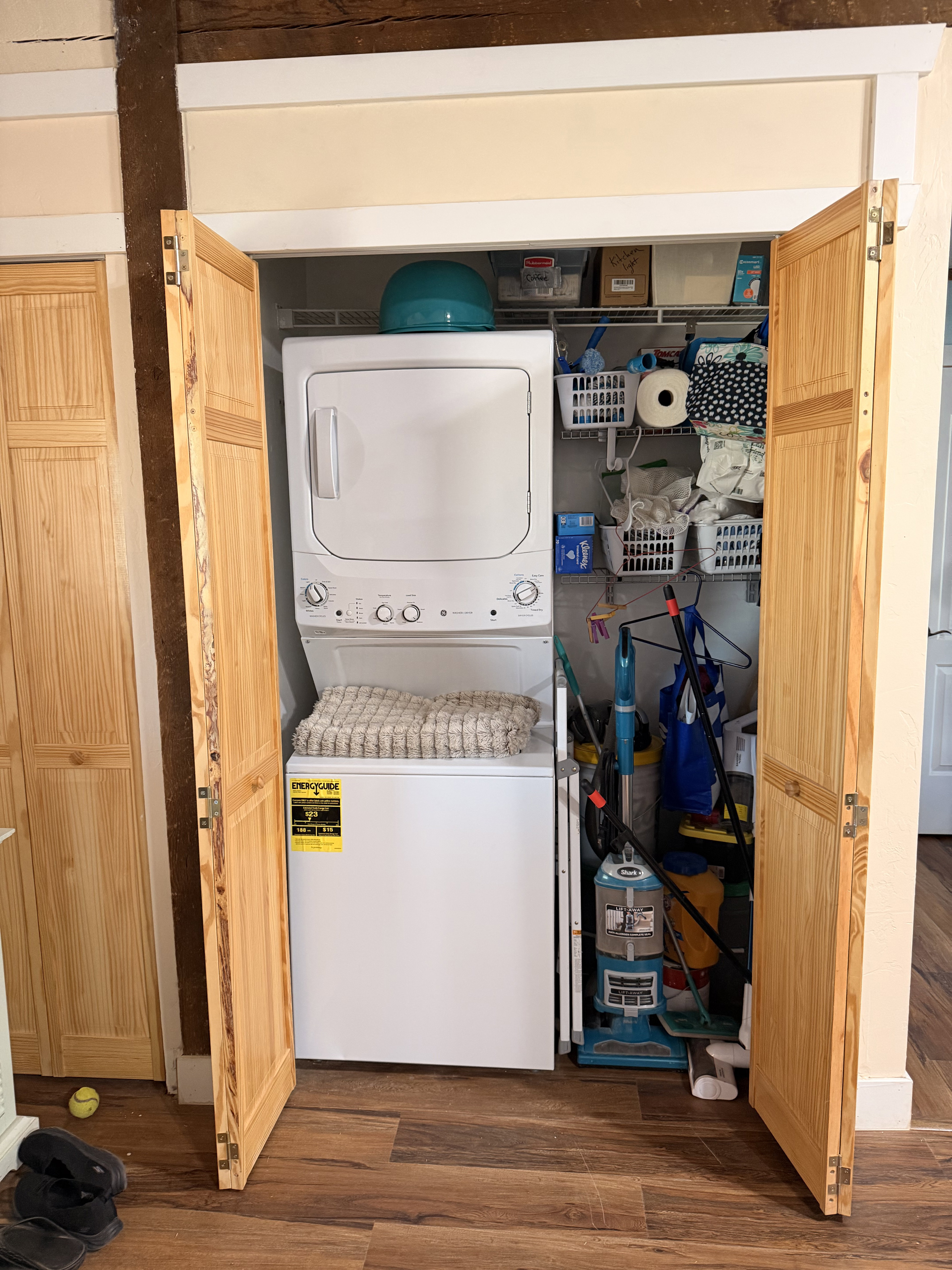 Integrated laundry closet featuring a stacked washer and dryer, bifold wood-finish doors, and overhead wire shelving