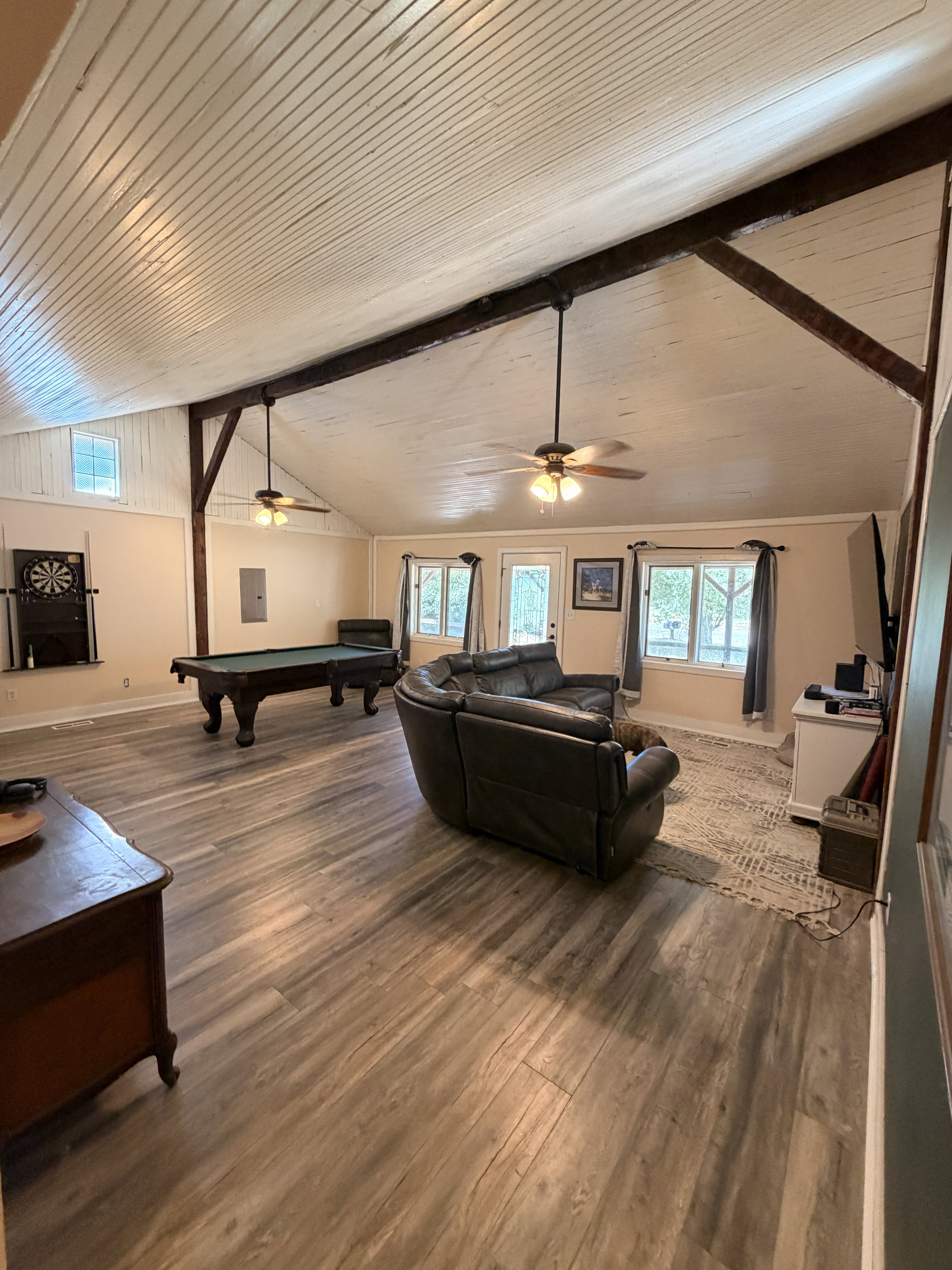 Spacious entertainment room featuring wood-finish flooring, a beadboard vaulted ceiling, exposed wood beams, and multiple windows