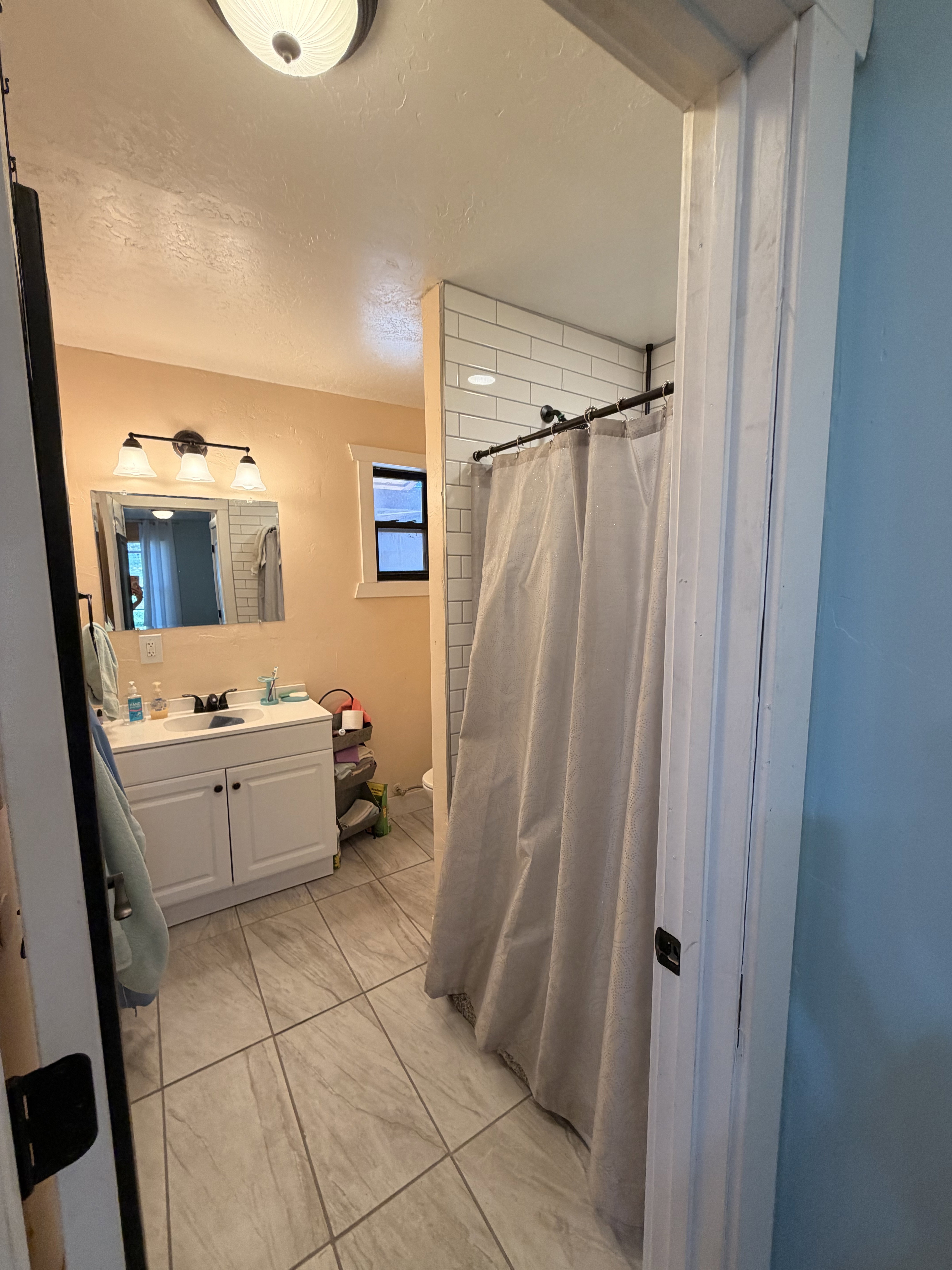 Bathroom featuring a white vanity with integrated sink, a three-light fixture, and subway tile shower surround
